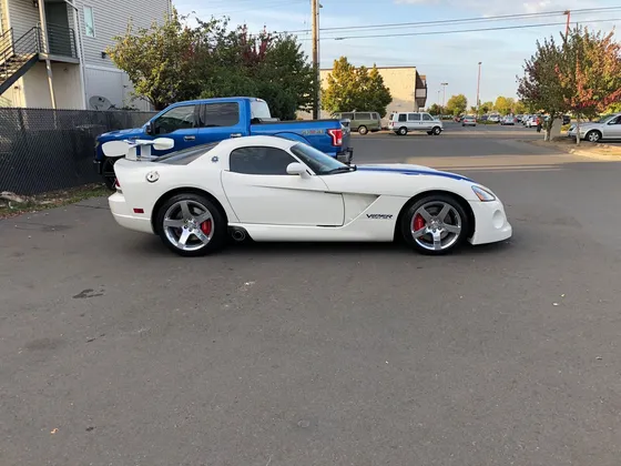 White Dodge Viper with blue stripes and chrome wheels parked in a lot, seen from the driver side