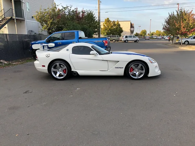 White Dodge Viper with blue stripes and chrome wheels parked in a lot, seen from the driver side