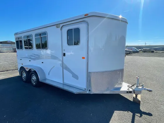 White two-horse trailer with a gray flame graphic parked on the lot in bright sun