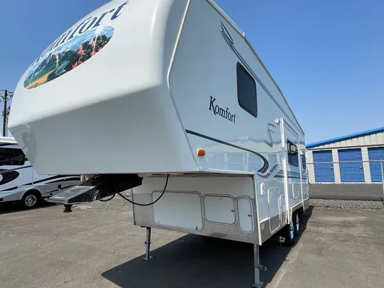 White Komfort fifth wheel trailer parked in the lot under a clear blue sky
