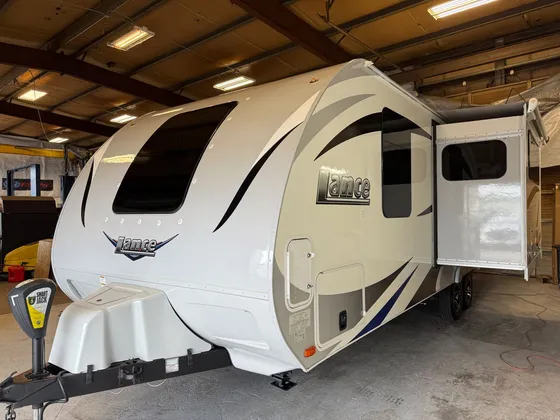 White Lance travel trailer with the slide-out open, parked inside the detail shop
