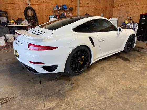White Porsche 911 Turbo S with black wheels and yellow calipers parked in the shop bay