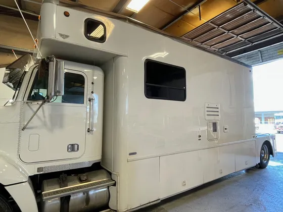 White motorhome built on a semi truck cab with a tall living body, parked in a shop bay