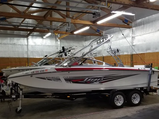 White Tige wake boat with red graphics on a trailer, a second boat parked behind it in the shop