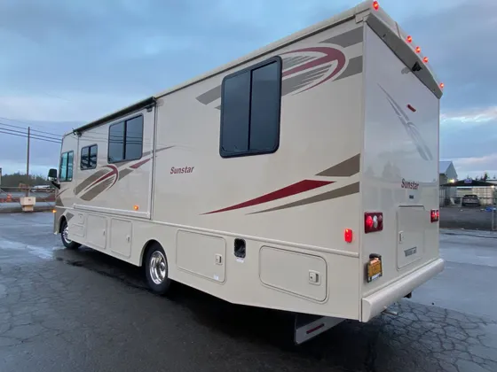 Tan Winnebago Sunstar motorhome with red stripes parked outside the shop at dusk